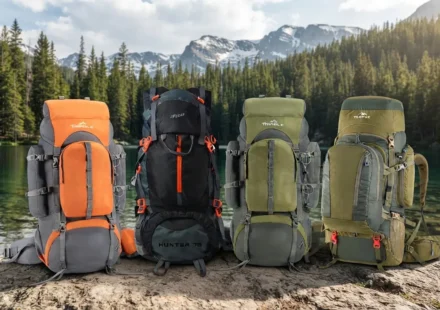 A collection of colorful rucksacks and hiking backpacks lined up on a scenic mountain rock overlooking a pristine alpine lake and forest."