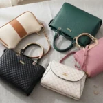 Collection of stylish women's handbags including quilted black, textured green, pink, and patterned designer purses arranged on a neutral fabric surface.