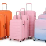 A vibrant collection of colorful orange, pink, and pastel gradient luggage suitcase sets lined up on a white background.